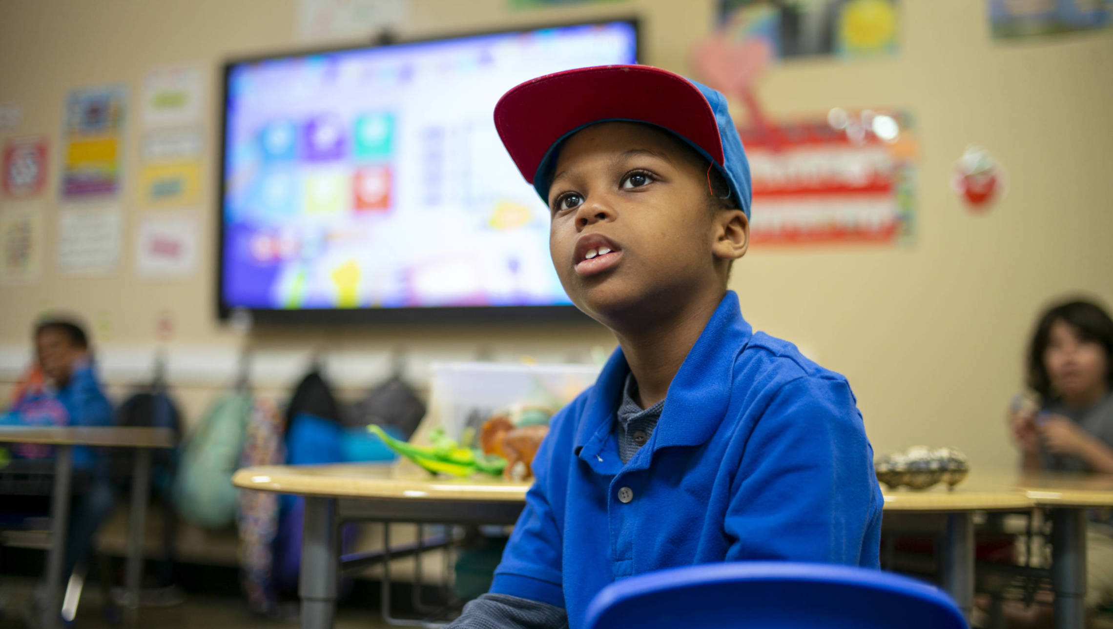Boy in blue shirt with hat on looking at teacher