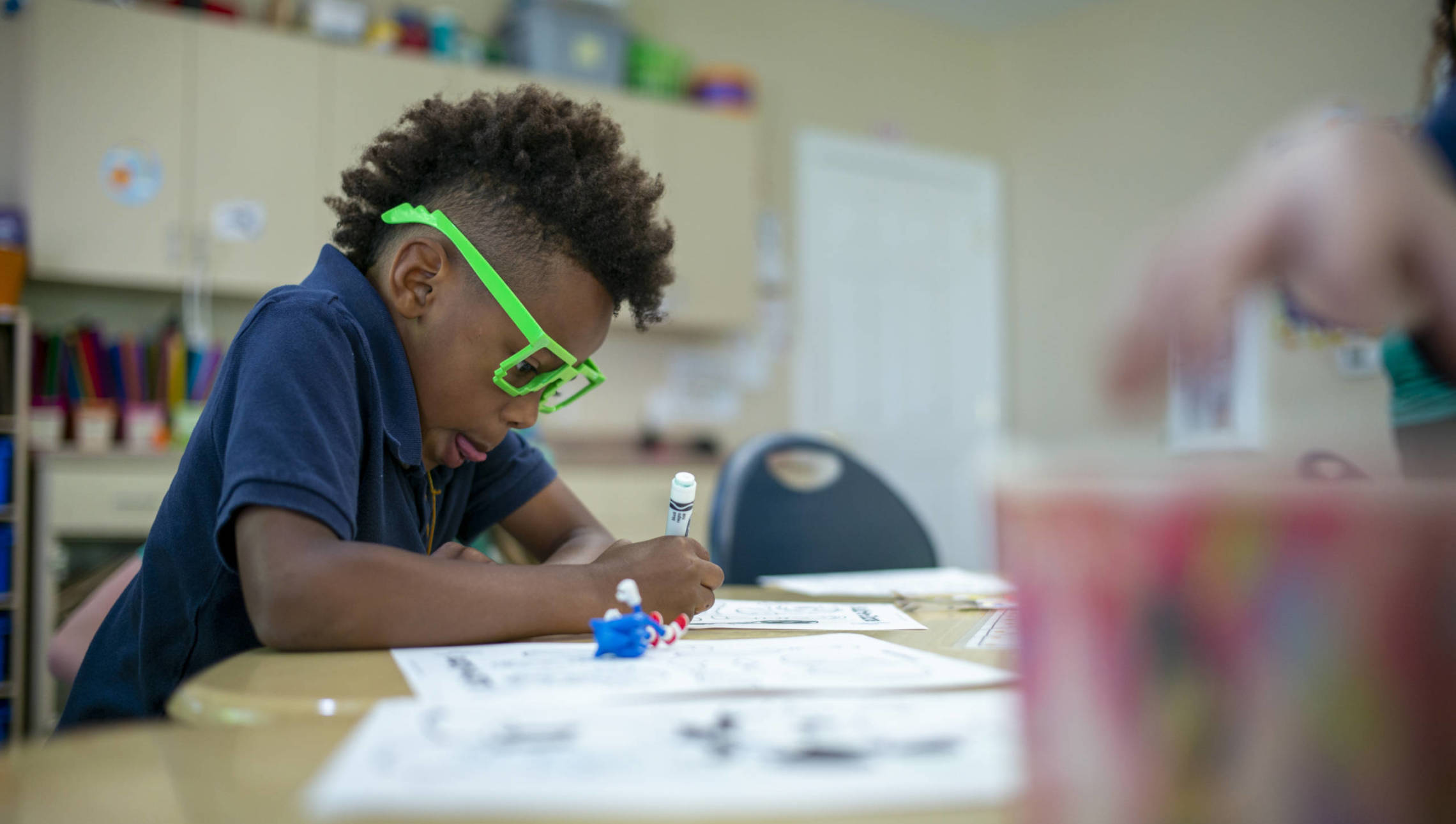 Boy in play glasses coloring in classroom